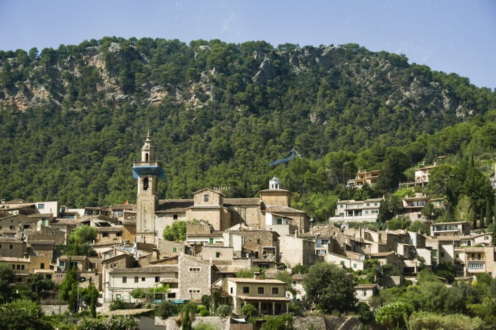 Scenic view of Valldemossa village with mountainous backdrop and lush greenery under a clear sky.